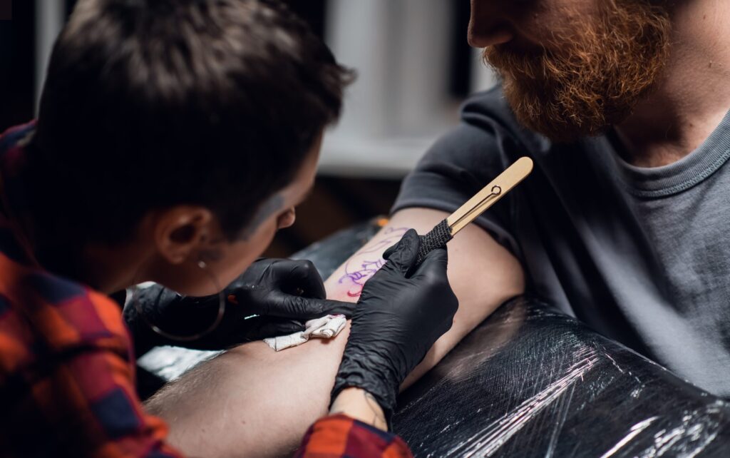 Tatérka dělající hand poke tetování na ruce klienta.