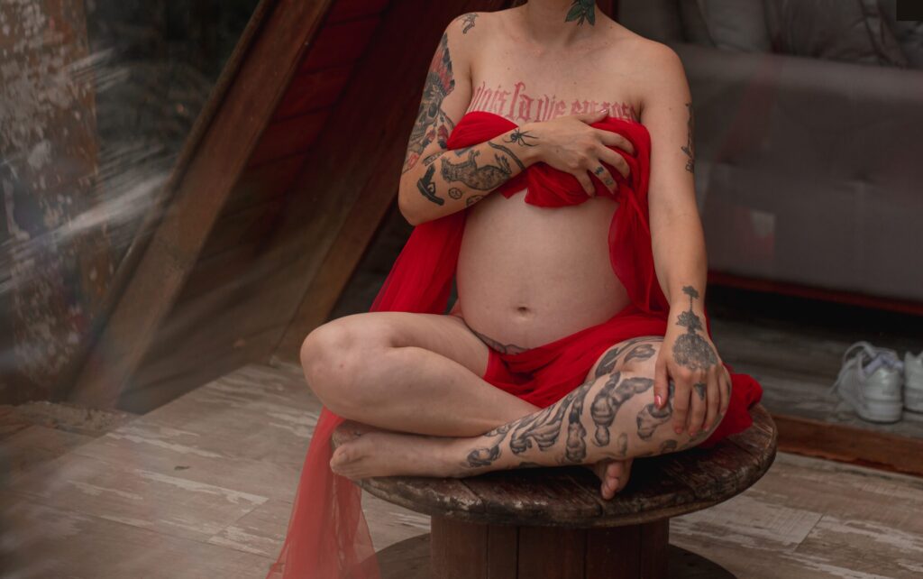 Těhotná potetovaná žena sedící v tureckém sedu.